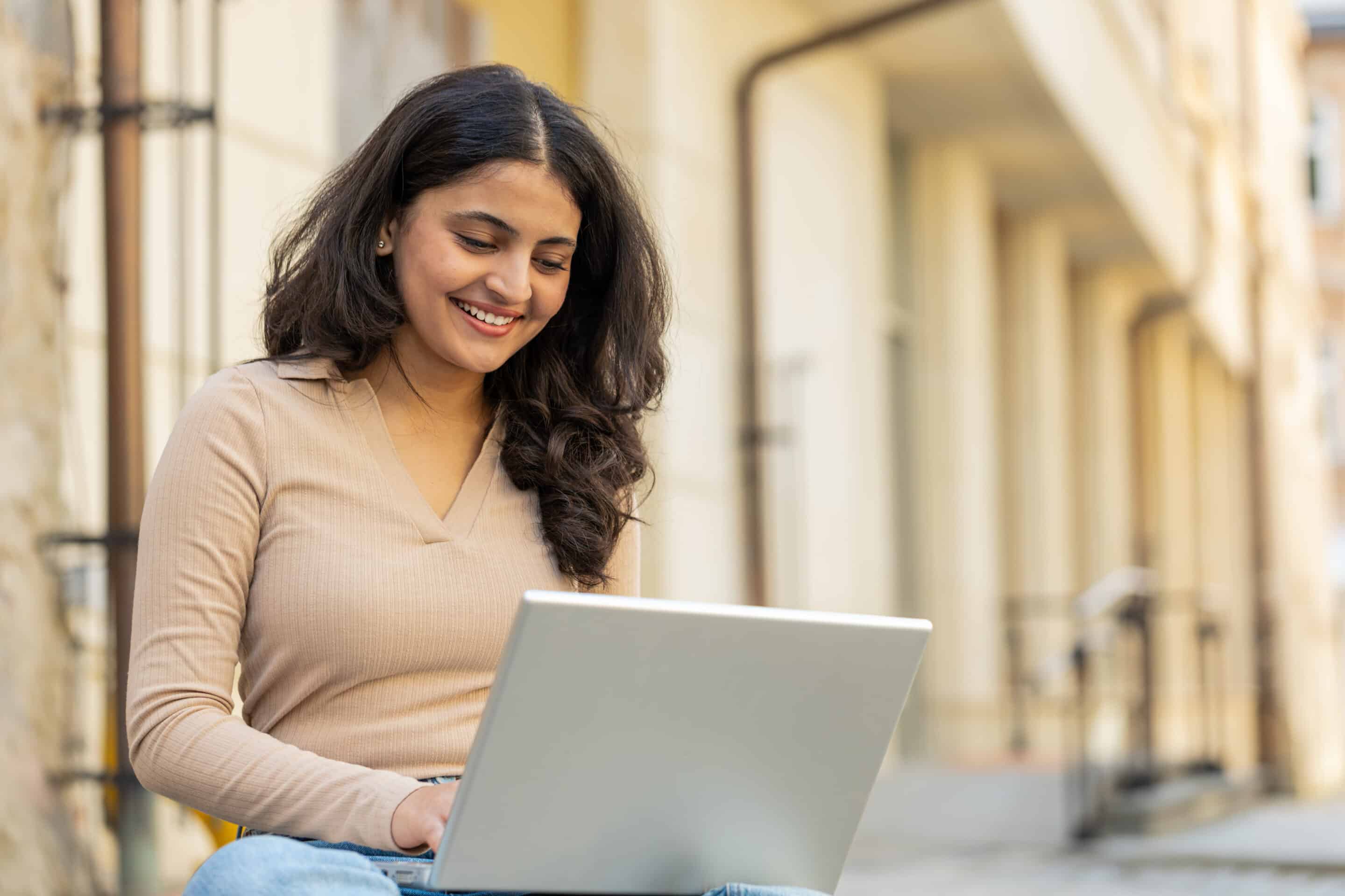 Woman freelancer working online distant job with laptop sitting on city street browsing website